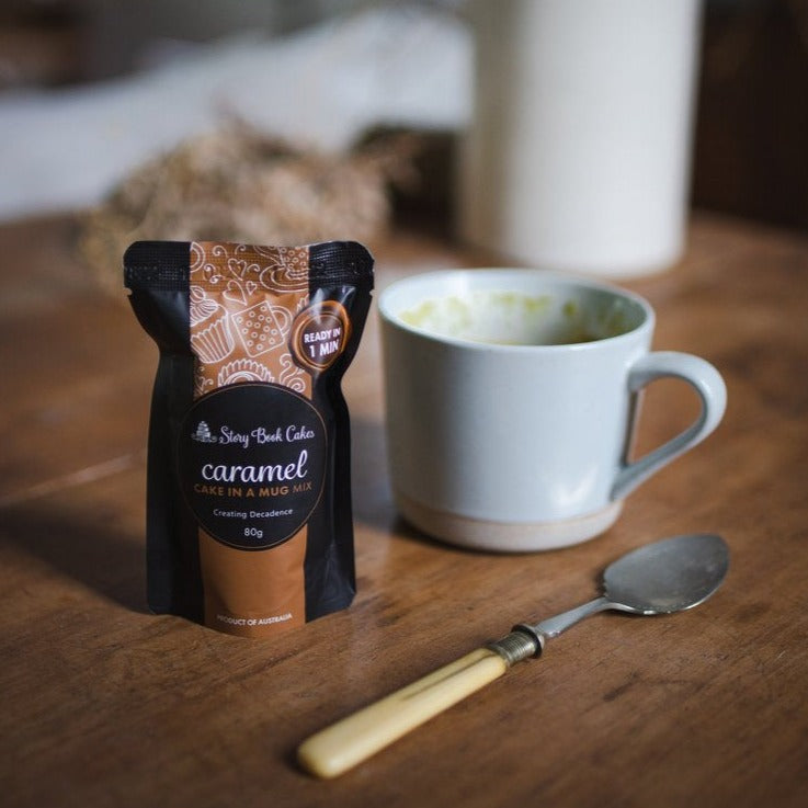 Caramel cake in a mug packet sitting on a bench next to a spoon and mug