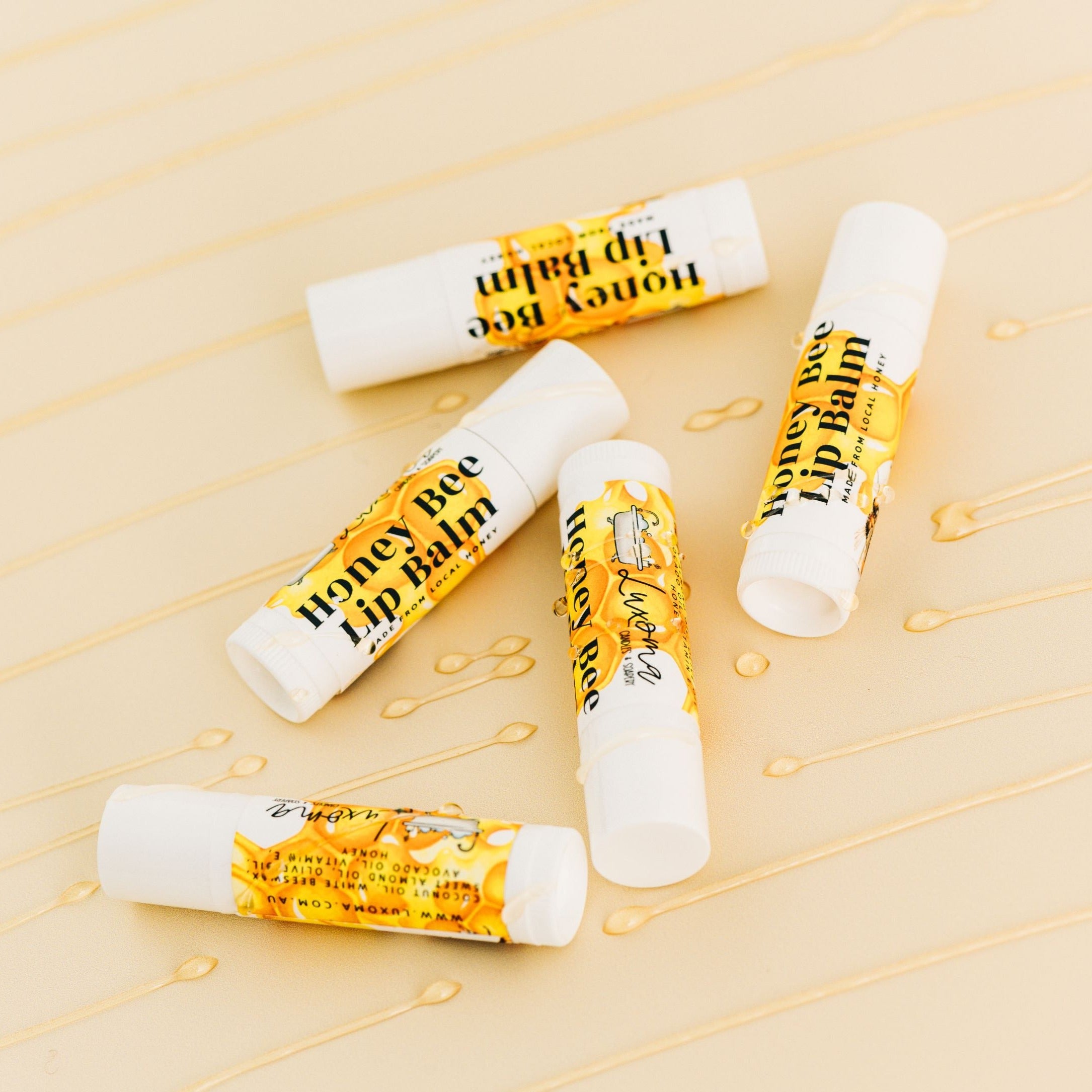 Honey Lip Balms on yellow desk with Honey drizzled over them